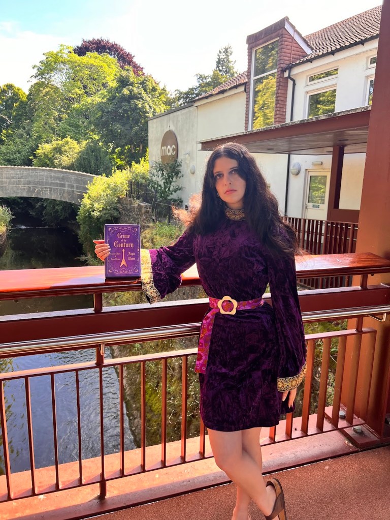 Angie Moon author of Crime of the Century Classic Rock and True Crime holding her book in a purple 70s inspired outfit: velvet bell sleeve dress with a purple Mary Quant inspired belt